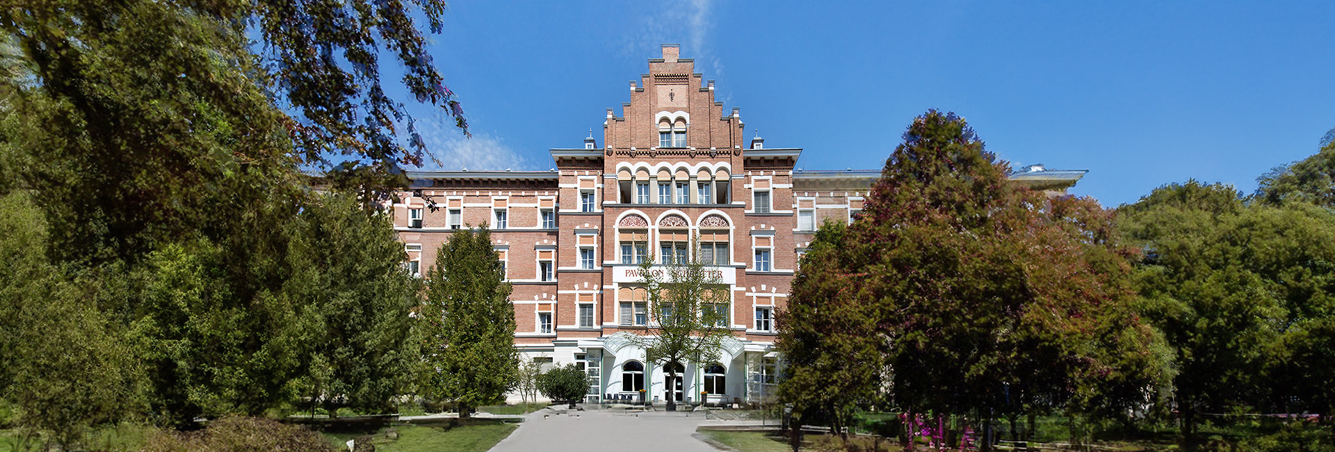 Außenansicht Reha-Zentrum Alland: Historisches Backsteingebäude, Bäume, Park